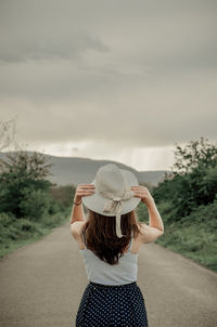 Rear view of woman wearing hat standing on road against sky