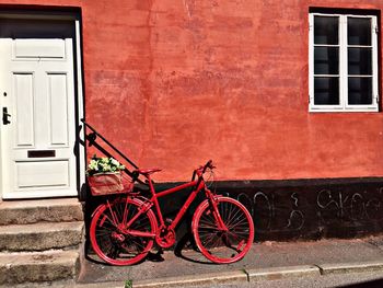 Red bicycle parked against house on sunny day
