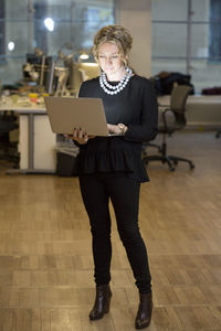 Full length of mature businesswoman using laptop in office