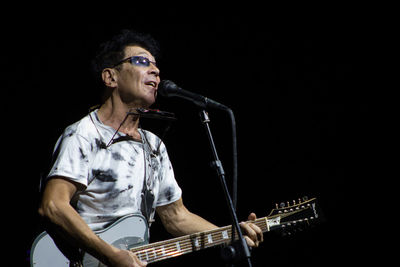 Full length of man playing guitar against black background