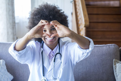 Doctor making heart gesture sitting on sofa