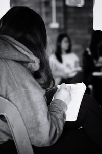 Rear view of woman writing in book while sitting on chair