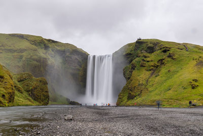 Scenic view of waterfall against cloudy sky - skogafoss