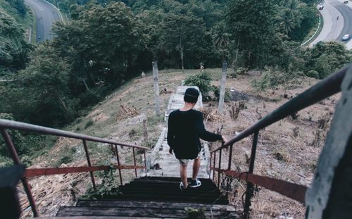 Rear view of man walking on staircase in forest