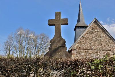 Low angle view of cross amidst trees against sky