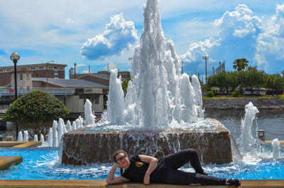 Portrait of young woman lying in front of fountain in city