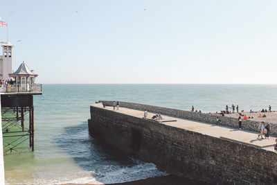 People on pier on sea against clear sky