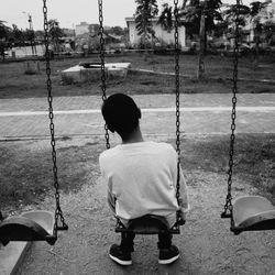 Rear view of man sitting on swing at playground