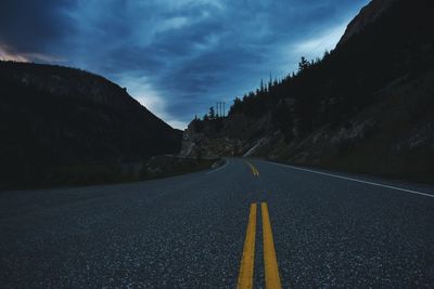 Empty road by mountains against sky at dusk