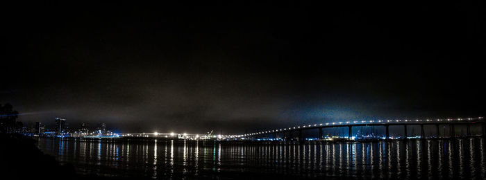 Illuminated bridge over river against sky at night