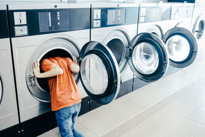 Boy looking in washing machine at laundromat