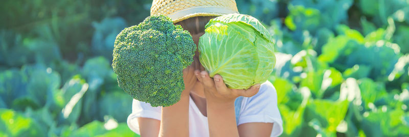 Cute girl holding cabbage and broccoli at farm