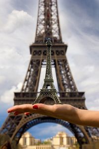 Cropped hand holding replica eiffel tower against eiffel tower in paris