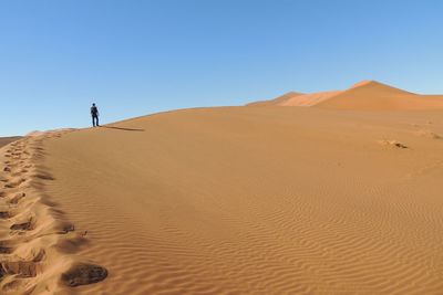 Low angle view of man walking at desert against clear blue sky
