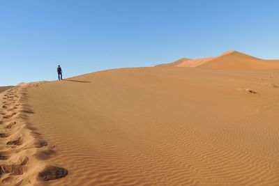 Low angle view of man walking at desert against clear blue sky