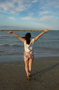 Rear view of woman standing at beach against sky