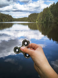 Cropped hand holding fidget spinner against lake