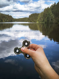 Close-up of hand holding water in lake against sky