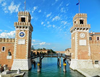 Clock tower in canal amidst buildings against sky