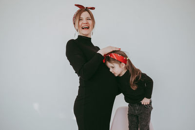 Daughter kissing pregnant mother abdomen against white background