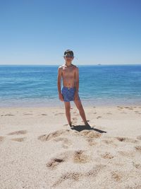 Portrait of shirtless boy standing at beach against clear sky during sunny day