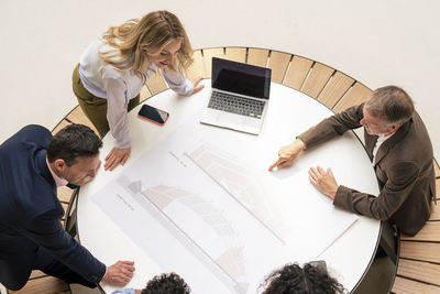 Senior businessman discussing over graph with colleagues in corridor