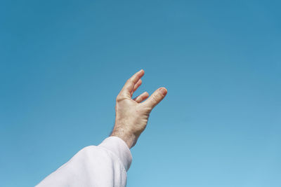 Low angle view of human hand against clear blue sky