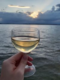 Close-up of hand holding glass of water against sky during sunset