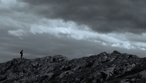 Hiker standing on rock against cloudy sky