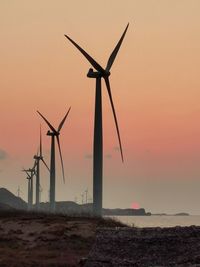 Windmills on beach against sky during sunset
