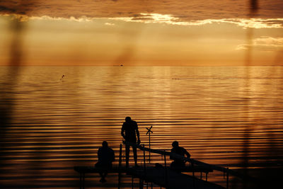 Silhouette people fishing in sea against sunset sky