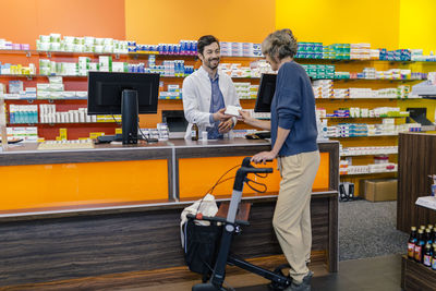 Pharmacist giving medicine to customer with wheeled walker in pharmacy