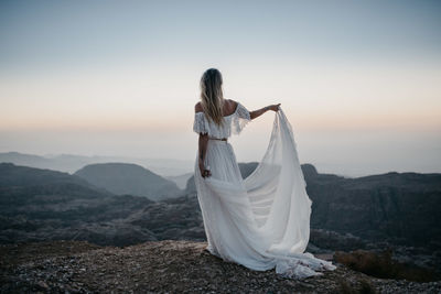 Woman with umbrella standing on mountain during sunset