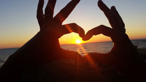 Silhouette hand by heart shape against sky during sunset