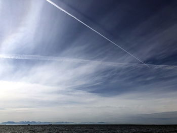 Low angle view of vapor trails over sea against sky