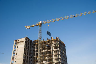 Low angle view of crane by building against clear blue sky