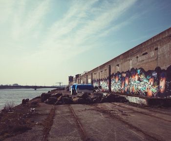 Graffiti on abandoned building by river against sky