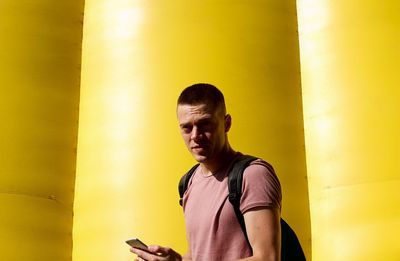 Portrait of man using mobile phone by yellow wall