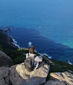 High angle view of man sitting on rock by sea