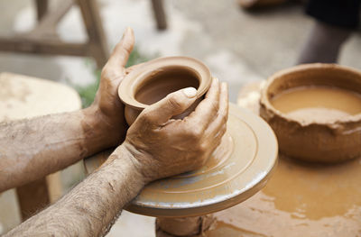 Cropped hands making clay pot on pottery wheel