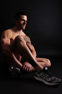 Shirtless athlete sitting against black background