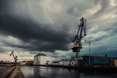 Cranes at harbor against cloudy sky