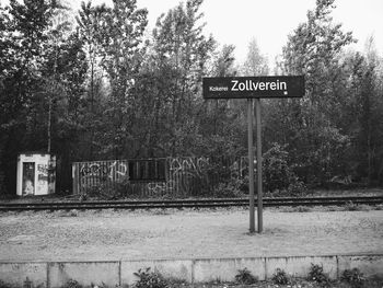 Road sign by trees against sky