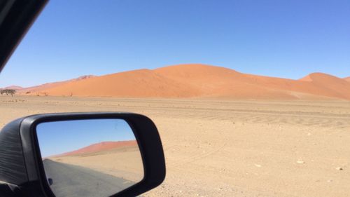 Scenic view of desert against clear blue sky and reflection in car mirror