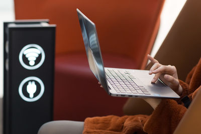 Midsection of woman using laptop while sitting indoors