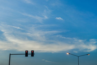 Low angle view of illuminated arrow symbols and street lights against blue sky during sunset