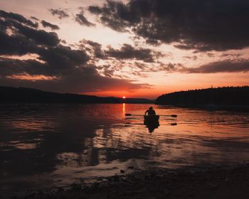 Scenic view of sea with man rowing boat against sky during sunset