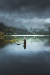 Rear view of man sitting on wooden post amidst lake