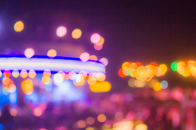Defocused image of illuminated lights against sky at night