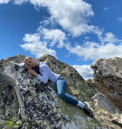 Rear view of man sitting on rock against sky
